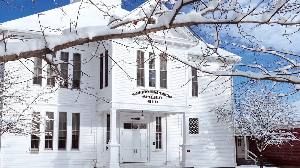 El edificio de la George Stevens Academy está cubierto de nieve y rodeado de ramas de árboles desnudos.