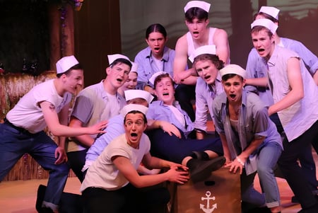 Estudiantes de George Watson’s College en uniformes blancos durante una representación teatral con telón de bambú.