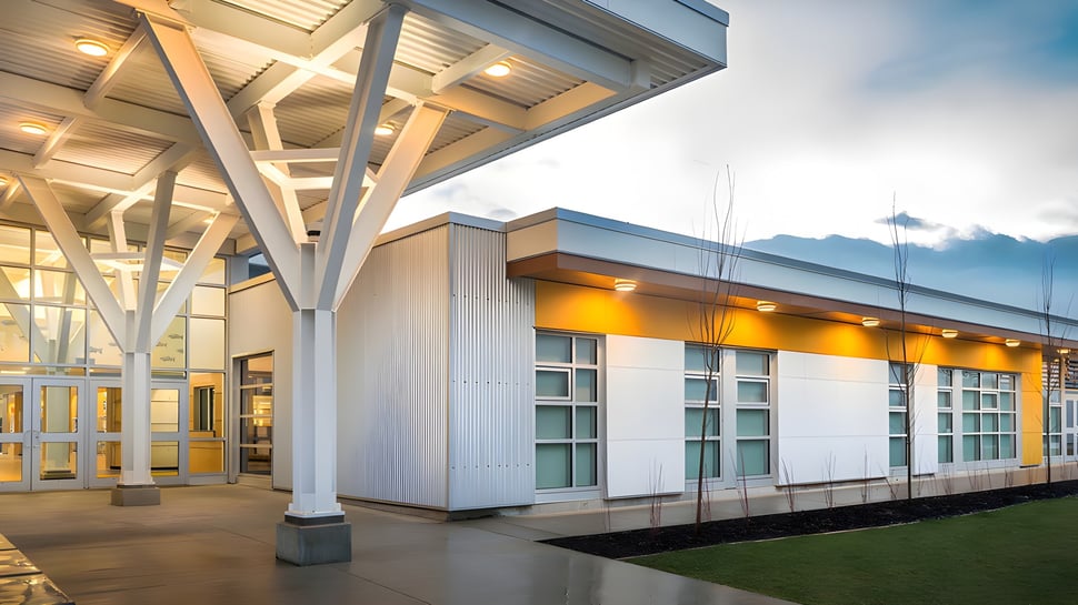 El moderno edificio de la Georges P. Vanier Secondary School con fachada de vidrio y camino cubierto bajo un cielo nublado.