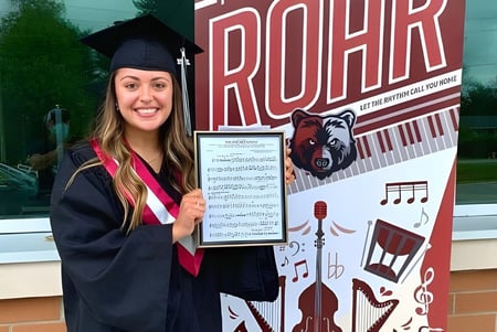 Una joven en toga de graduación se encuentra frente al gran letrero ROAR en la Georgian Bay District Secondary School.