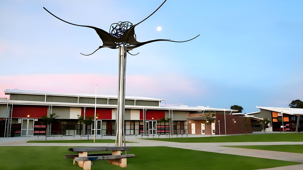 Una gran escultura de metal en forma de mariposa se encuentra sobre un alto poste frente al moderno complejo de edificios del Gilmore College.