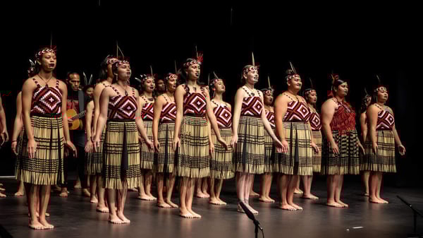 Un grupo de alumnas de la Gisborne Girls' High School está en el escenario con trajes tradicionales inspirados en tribus con patrones elaborados.