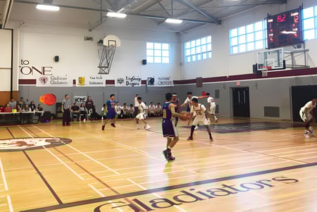 Estudiantes de la Gladstone Secondary School juegan activamente un partido de baloncesto en un gimnasio luminoso con grandes ventanas.