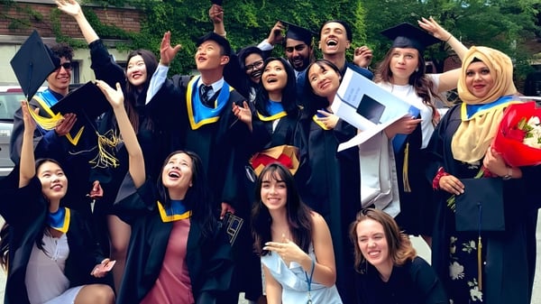 Un grupo de graduados en togas coloridas celebra frente a un edificio de ladrillo en el campus del Glebe Collegiate Institute.