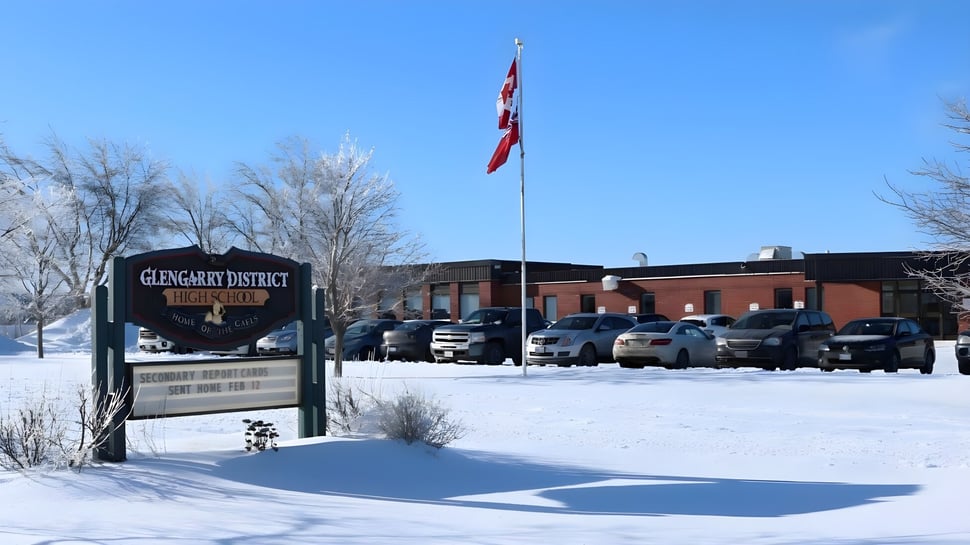 Una imagen invernal nevada con el cartel de Glengarry District High School y un edificio con bandera al fondo.
