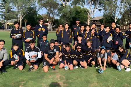 El equipo deportivo de la Glenunga International High School posan juntos en un campo cubierto de hierba con árboles al fondo.