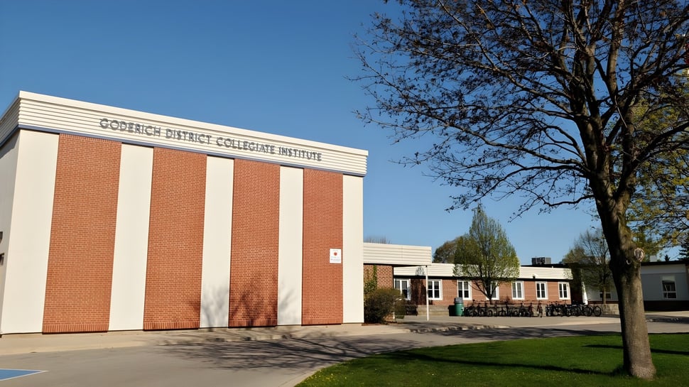 El edificio de ladrillo del Goderich District Collegiate Institute está rodeado de un prado con un árbol en primer plano.