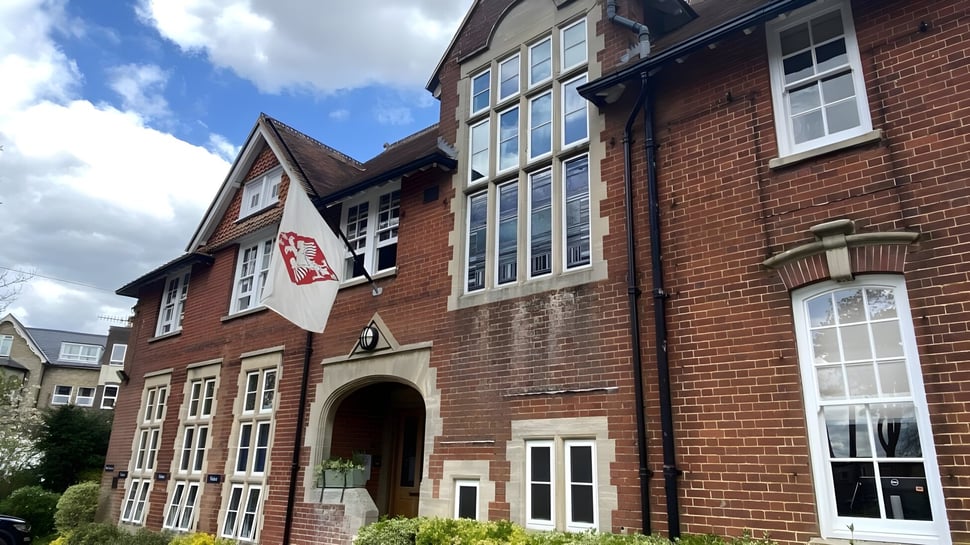 El edificio de ladrillo de varios pisos de la Godolphin School con grandes ventanas y una entrada principal abovedada frente a un cielo nublado.