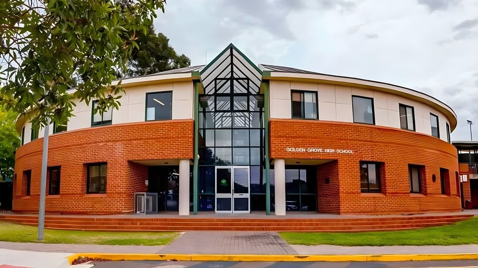 El moderno edificio principal de la Golden Grove High School con estructura de vidrio triangular en la entrada y entorno verde.