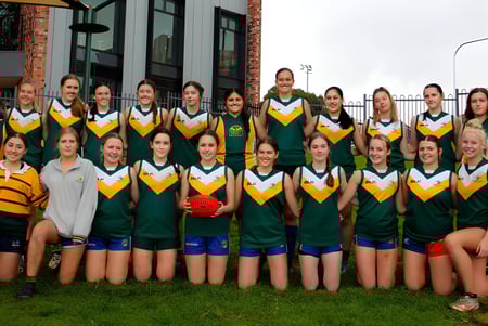 Un grupo de estudiantes de la Golden Grove High School posan con la camiseta deportiva verde y amarilla frente a un edificio de ladrillo al aire libre.