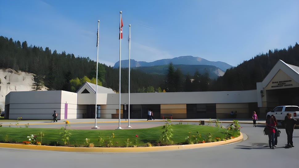 El moderno edificio de varios pisos de la Golden Secondary School con banderas en el techo se encuentra frente a montañas boscosas y césped bien cuidado.