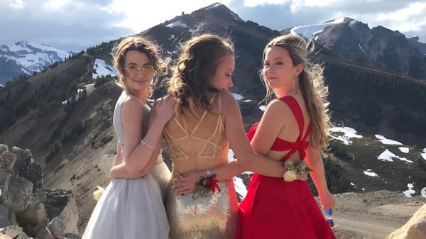 Tres alumnas de la Golden Secondary School están en traje de baño frente a montañas nevadas y un cielo nublado.