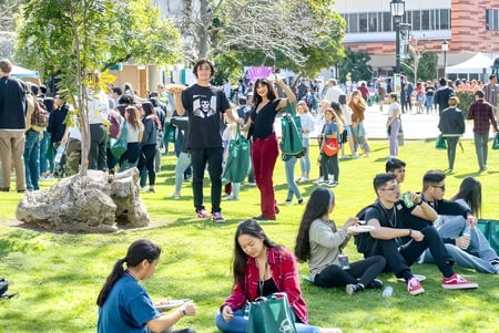 Estudiantes del Golden West College están sentados y caminando en el animado área exterior entre árboles y edificios.