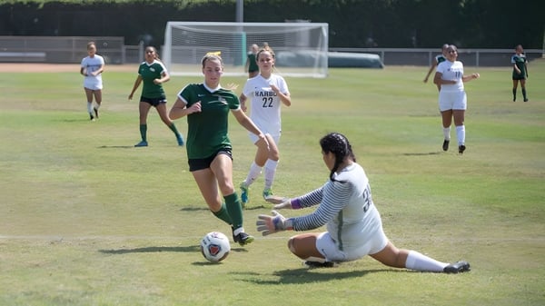 Estudiantes del Golden West College juegan un partido de fútbol en el campo deportivo con un intenso duelo entre dos jugadores.