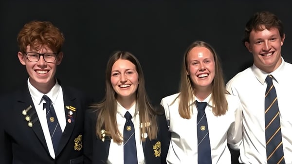 Cuatro estudiantes en uniforme escolar posan sonriendo frente a un fondo oscuro en el campus de la Gore High School.