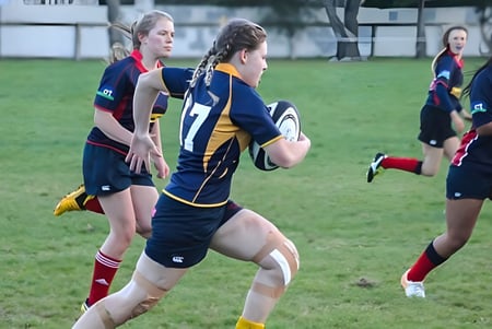 Un grupo de jugadoras de rugby de la Gore High School lucha en el campo durante un partido.