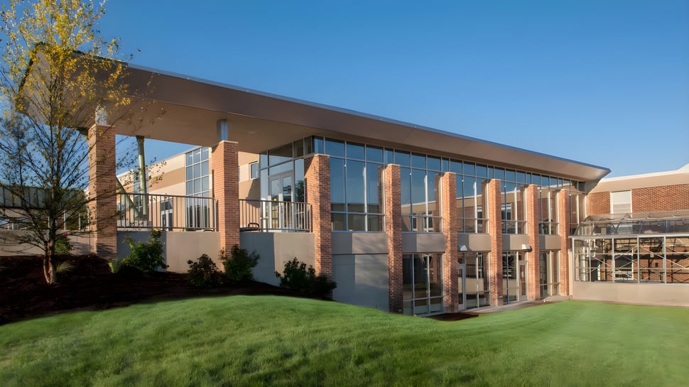 El moderno edificio de varios pisos de la Grand Rapids Christian High School con fachada de vidrio se encuentra en un área verde bajo un cielo despejado.