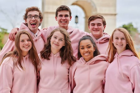 Un grupo de estudiantes con sudaderas rosas está junto a un edificio en el campus de la Grand Rapids Christian High School.