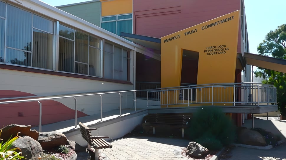 El moderno edificio de Grant High School muestra una entrada con rampa y un paisaje natural con piedras y plantas.