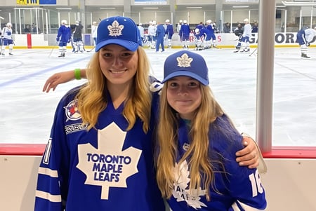 Dos estudiantes de la Gravenhurst High School llevan camisetas de los Toronto Maple Leafs y posan frente a una arena de hockey.