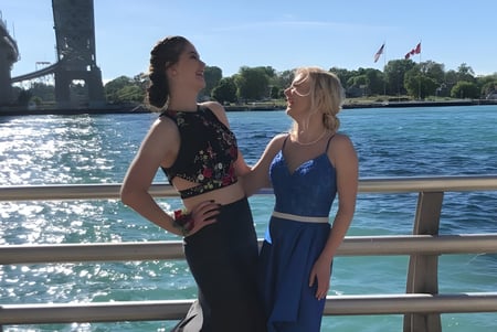 Dos estudiantes de la Great Lakes District Secondary School están en un muelle de madera con agua y un puente al fondo.