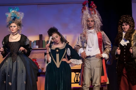 Cuatro estudiantes disfrazados del Greater Essex County District School Board se presentan en un escenario con un fondo colorido.