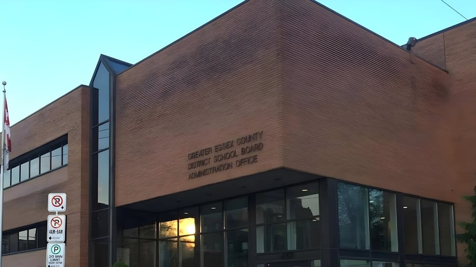 El gran edificio de ladrillo con ventanas de vidrio del Greater Essex County District School Board bajo un cielo azul claro.