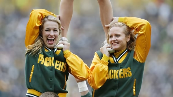 Dos estudiantes del Green Bay Area Public School District animan al aire libre con camisetas deportivas verdes y amarillas.