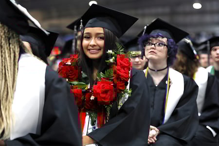 Una joven en toga de graduación sostiene un ramo de rosas en la ceremonia de graduación del Green Bay Area Public School District.