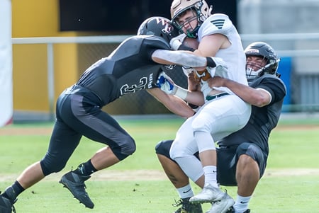 Dos jugadores de fútbol americano de la Green Fields High School realizan una escena de tackle en el campo.