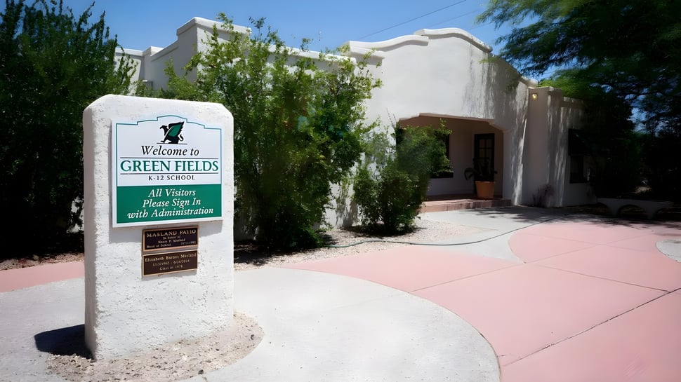 El cartel de bienvenida de la Green Fields High School está frente a un edificio blanco y rodeado de vegetación verde.