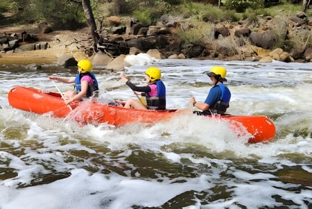Estudiantes del Greenwood College navegan con chalecos salvavidas de colores y cascos en una balsa roja por un río salvaje.