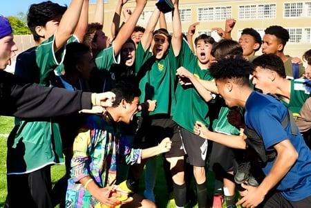 Un grupo de estudiantes de la Greenwood Secondary School en uniformes escolares verdes celebra juntos frente al edificio escolar.