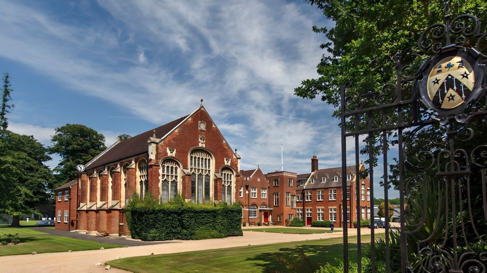 El histórico edificio de ladrillo de Gresham’s School está rodeado de un paisaje verde y está enmarcado por una decorativa puerta de hierro forjado.