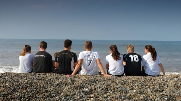 Un grupo de personas está sentado en una playa de grava con vista al mar tranquilo en el terreno de Gresham’s School.