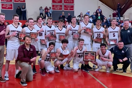 Estudiantes y entrenadores de la Groton-Dunstable Regional High School celebran con trofeos en la cancha de baloncesto su victoria.