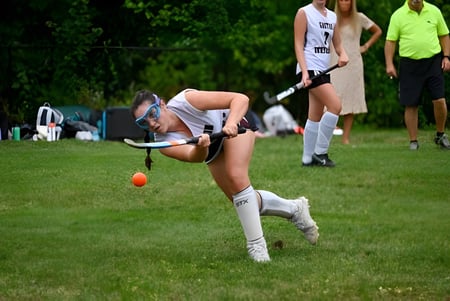 Un estudiante del Groton-Dunstable Regional School District hace un pino en un campo con otros estudiantes al fondo.