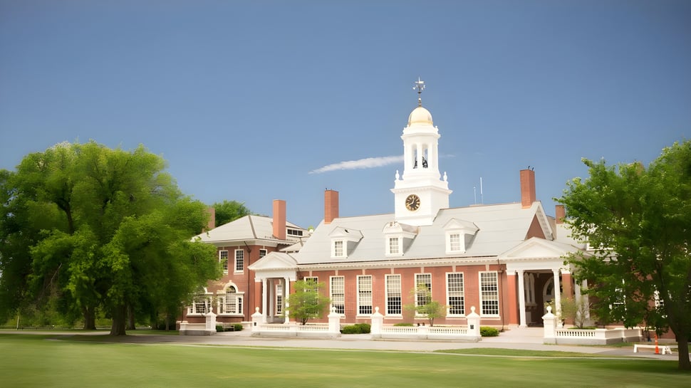 El edificio de ladrillo con torre del reloj blanca en el campus de la Groton School está rodeado de árboles y un césped verde.