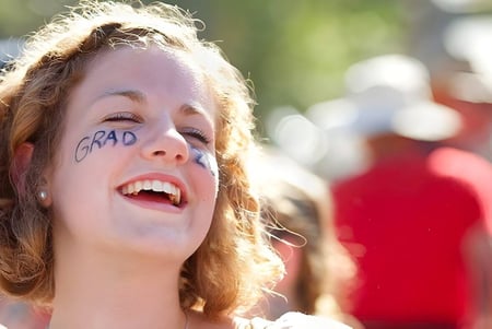 Una joven con cabello rizado y un diseño de GRAD en la cara celebra su graduación en la Gulf Islands Secondary School.