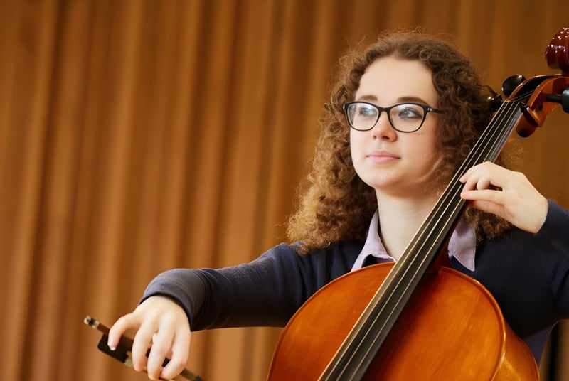 Una estudiante de Haberdashers' Monmouth Schools toca el cello en un escenario con un telón de fondo.