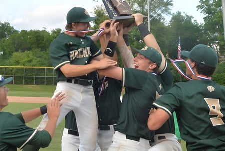 Un grupo de estudiantes de la Hackett High School en uniformes verdes celebran juntos en el campo de béisbol.
