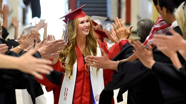 Una graduada en toga roja es celebrada por una multitud animada en el campus de la Hackett High School.
