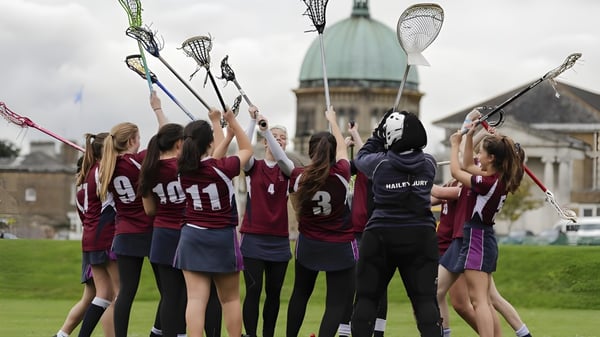 Un grupo de jóvenes atletas con palas de lacrosse está frente a un edificio histórico en el campus de la Haileybury School.