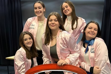 Un grupo de jóvenes mujeres con atuendos rosas a juego está frente a un fondo oscuro en el campus de la Haliburton Highlands School.