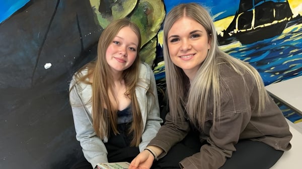 Dos estudiantes de la Haliburton Highlands School posan frente a un colorido mural abstracto.
