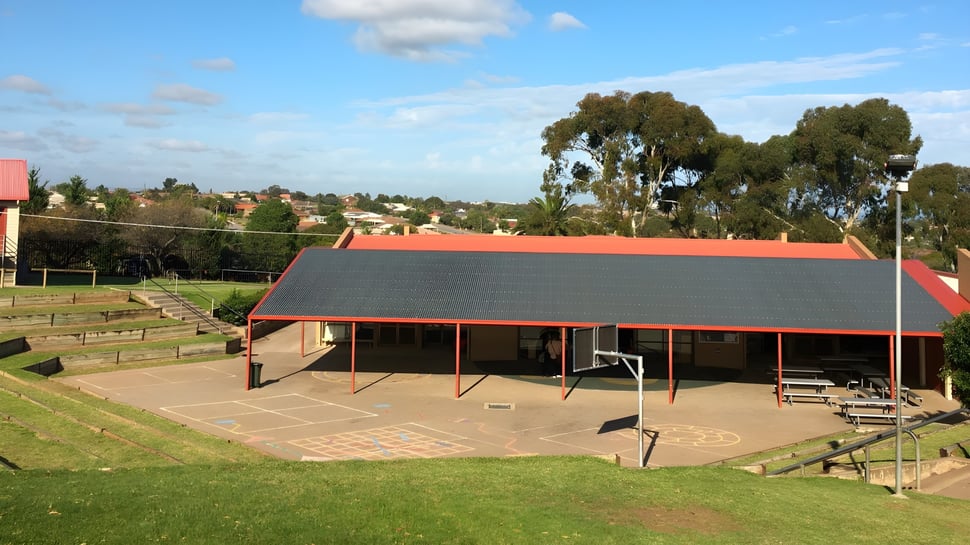 Una zona verde al aire libre con un área cubierta en el terreno de la Hallett Cove School bajo un cielo azul.