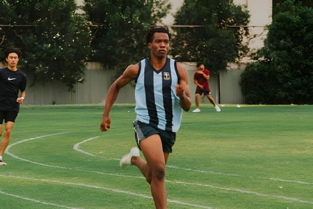 Un estudiante del Hamilton Secondary College corre en un campo verde durante una actividad deportiva.