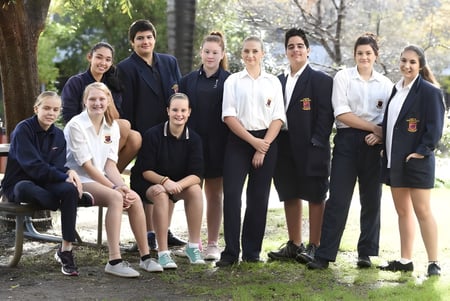 Un grupo de estudiantes está de pie y sentados juntos en un espacio exterior natural de Hampton Senior High School.
