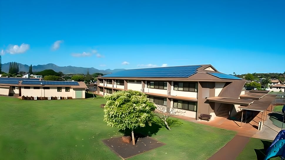 El edificio de Hanalani Schools muestra paneles solares en el techo y se encuentra en un entorno verde con montañas al fondo.