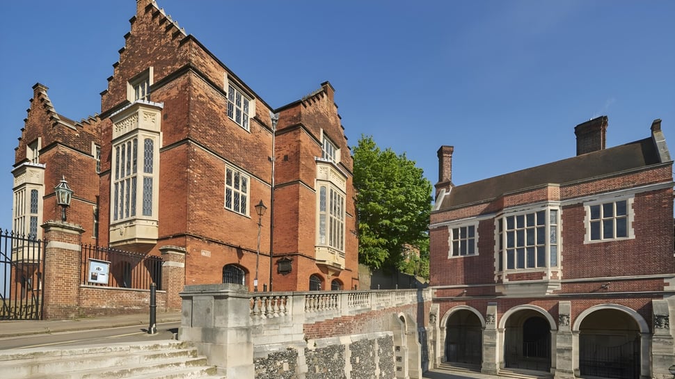 El histórico edificio principal de la Harrow School con detalles artísticos y rodeado de vegetación verde bajo un cielo claro.